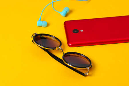 Women's accessories and gadgets on a yellow background. Earphones, stylish round sunglasses, smartphone on a yellow backgroundの写真素材