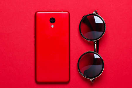 Fashionable glasses and smartphone on red background. Women's accessories