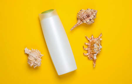 Bottle of shampoo with shells on a yellow background. Top view