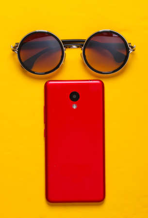 Fashionable glasses and smartphone on yellow background. Women's accessoriesの写真素材