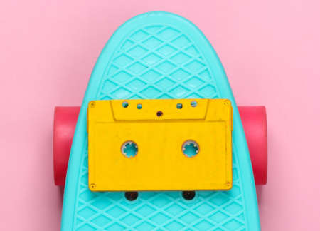 Cruiser board with audio cassette on a pink pastel background. 80s fun. Top viewの写真素材