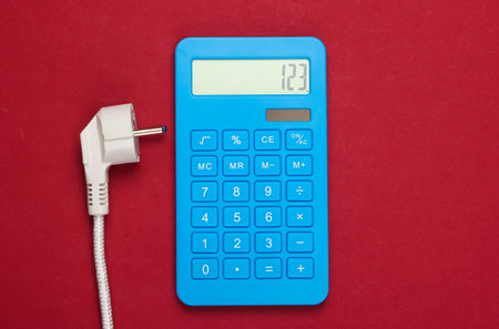 Calculator with a power plug on red background. Calculation of energy consumption costs. Top view