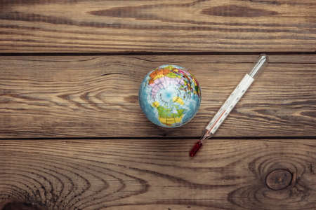 Global warming concept. Globe with thermometer on a wooden background. Top view