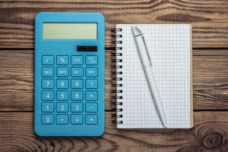 Calculator with notebook on a wooden background. Top view