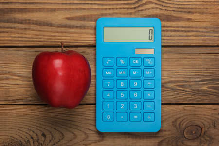 Calculator with red apple on a wooden background. Top viewの写真素材