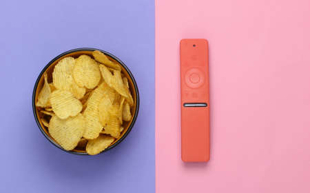 Movie time. Tv remotes and bowl with chips on purple pink pastel background. Top view