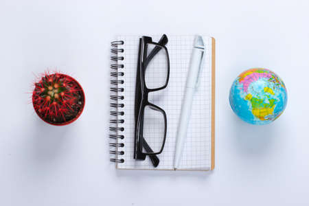 Notebook with pen, glasses, cactus, globe on white background. Working space. Top viewの写真素材