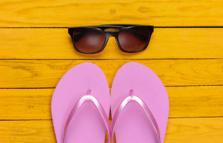 Flip flops with sunglasses on a yellow wooden background. The concept of a beach holiday, resort. top viewの写真素材