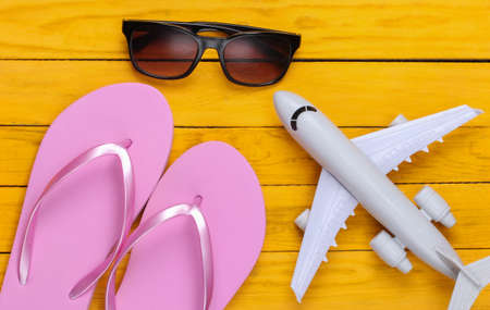 Concept of a resort, beach holiday or tourism. Flip flops, figurine of a passenger plane, sunglasses on a yellow wooden background. top view. flat layの写真素材