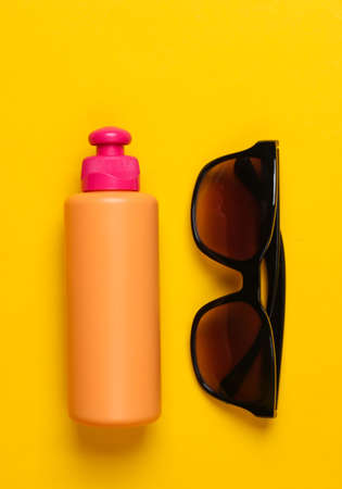 Bottle of sunblock with sunglasses on a yellow background. Beach Vacation Concept. top viewの写真素材