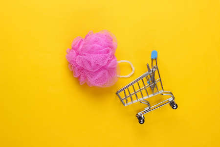Supermarket trolley with bath sponge on yellow background. top view