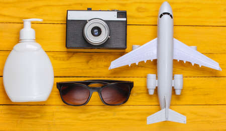 Concept of a resort, beach holiday or tourism. Figurine of a passenger plane, sunglasses, sunblock, camera on yellow wooden background. top view. flat layの写真素材