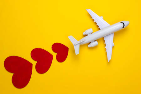 Air travel lover. Airplane figurine with red hearts on yellow background. top viewの写真素材
