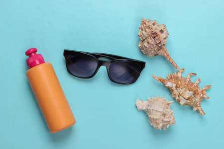 Bottle of sunblock with sunglasses, seashells on blue background. Beach Vacation Concept. top viewの写真素材