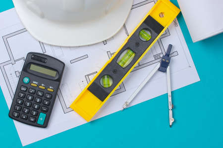 Hard hat with building level, calculator, compass, blueprint on blue studio background. Engineering, construction equipment. top viewの写真素材