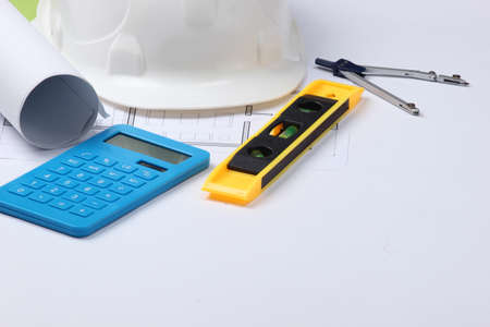 Hard hat with building level, calculator, compass, blueprint on white studio background. Engineering, construction equipment.の写真素材