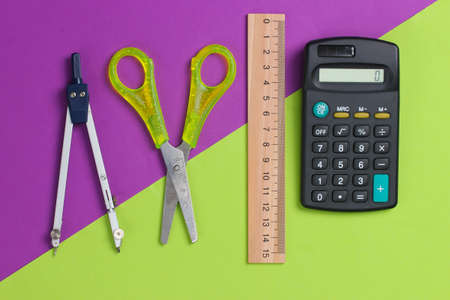 Stationery (school) scissors, calculator, compass, ruler on green purple background. school...
