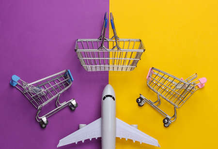 Air delivery, shopping concept. Mini supermarket trolleys, basket and airplane figurine on yellow purple background. top viewの写真素材
