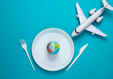 Eco concept. plastic pollution. Globe on plastic plate, fork and knife, airplane. blue background. top viewの写真素材