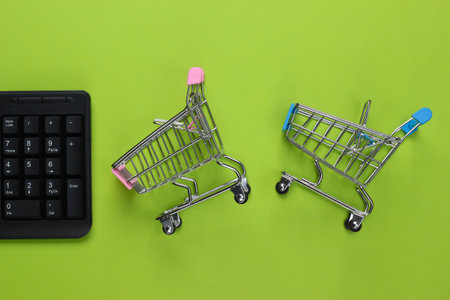 online shopping. PC keyboard with supermarket trolleys on green background. top view. flat lay