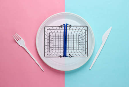 Supermarket basket in plastic plate with fork and knife on pink blue pastel background. food purchases. top viewの写真素材