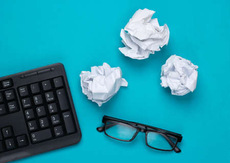 office flat lay. PC keyboard, crumpled paper balls, glasses on a blue studio background. top viewの写真素材