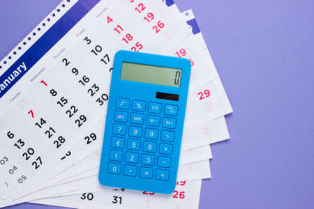 Calculator with a monthly calendar on a purple background. top view