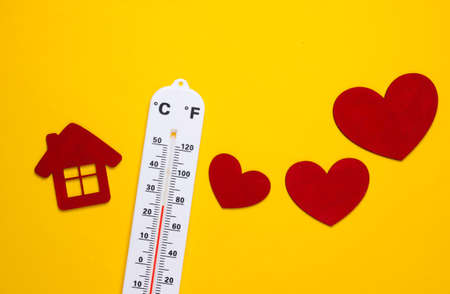 Weather thermometer and house figurine, heart on yellow background. climate control. top view
