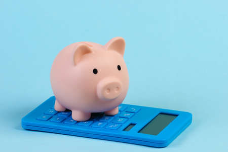 Piggy bank with calculator close-up on blue pastel background. Calculation of the family budget, saving. minimalismの写真素材