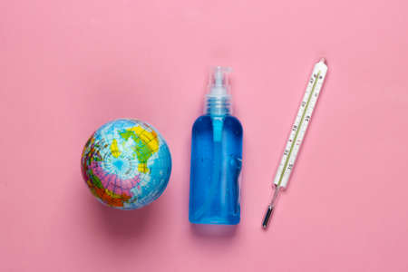 Antiseptic bottle, thermometer and globe on pink background. Disinfectant. Global pandemic covid-19....