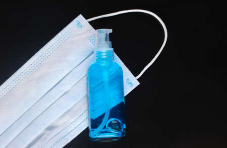 Antiseptic bottle with blue liquid and medical face mask on black background. Infection prevention and controlの写真素材
