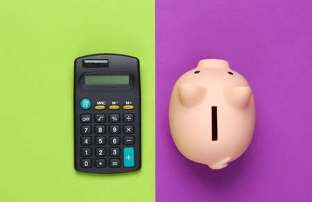 Piggy bank and calculator on purple green background. Minimalistic studio shot. Overhead view. Flat lay.の写真素材