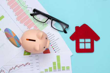 Piggy bank with graphs and charts, house figure on a blue background. Housing Cost Analysis. Top viewの写真素材