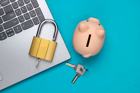 Laptop with keys and lock, piggy bank on a blue background. Top view