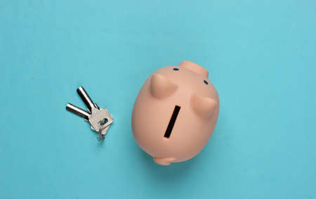 Piggy bank with house keys on a blue background. Payment of rent for housing, save money for house....