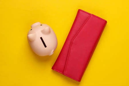 Piggy bank and wallet on yellow background. Minimalistic studio shot. Overhead view. Flat lay.