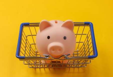 Supermarket basket with piggy bank on a yellow background. Shopping conceptの写真素材
