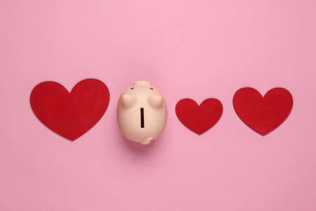 Piggy bank and hearts on pink pastel background. Minimalistic studio shot. Overhead view. Flat lay.