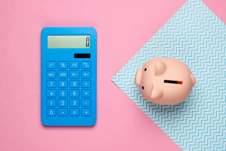 Piggy bank and calculator on blue pink background. Minimalistic studio shot. Overhead view. Flat...