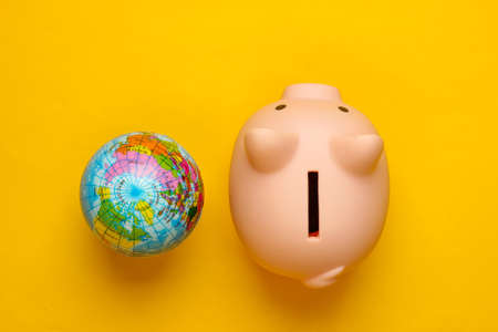 Piggy bank and globe on yellow background. Minimalistic studio shot. Overhead view. Flat lay.