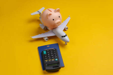 Save up for air travel. Piggy bank with toy airplane, passport, calculator on yellow background.の写真素材