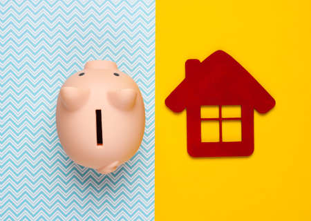 Save for housing. Piggy bank and house figure on yellow blue background. Minimalistic studio shot. Overhead view. Flat lay.の写真素材