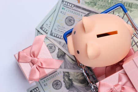 Supermarket basket with piggy bank, gift boxes on hundred dollar bills. Top view