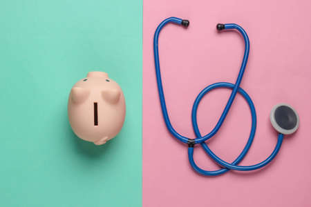 Medicine still life. Piggy bank with stethoscope on pink blue background. Minimalism. Top viewの写真素材