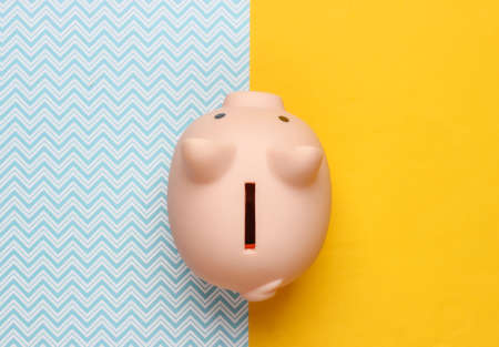 Piggy bank on yellow blue background. Minimalistic studio shot. Overhead view. Flat lay.
