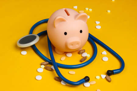 Medicine still life. Piggy bank with stethoscope, pills on yellow background.の写真素材