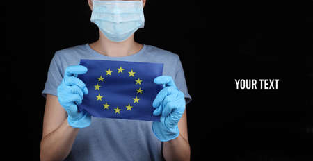 Woman in face mask and gloves holding EU flag on black background.の写真素材