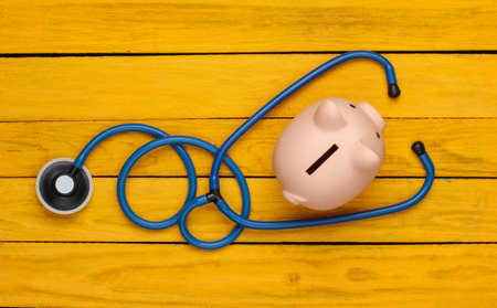 Medicine concept. Stethoscope with piggy bank on a yellow wooden background. Top viewの写真素材
