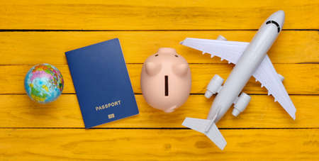 Travel or emigration. Passport with piggy bank, globe and plane on a yellow wooden background. Top view. Flat layの写真素材