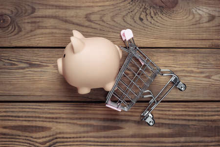 Shopping concept, economy. Piggy bank with supermarket trolley on wooden background. Top viewの写真素材